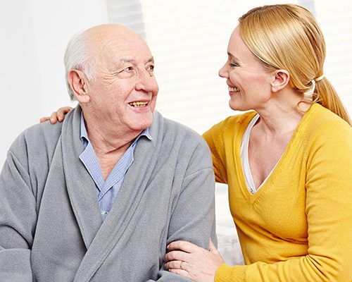 Caretaker and an elderly man smiling at each other